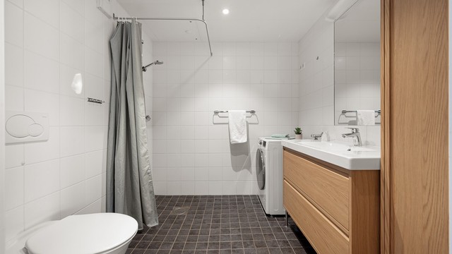 Badet har varmekabler i gulvet og er utstyrt med vegghengt toalett og dusjhjørne.