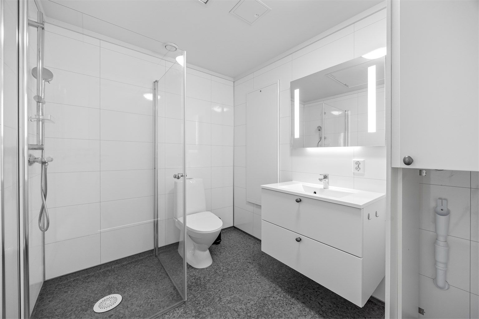 Lyst og pent baderom med opplegg til vaskemaskin, dusjhjørne, servant og toalett.