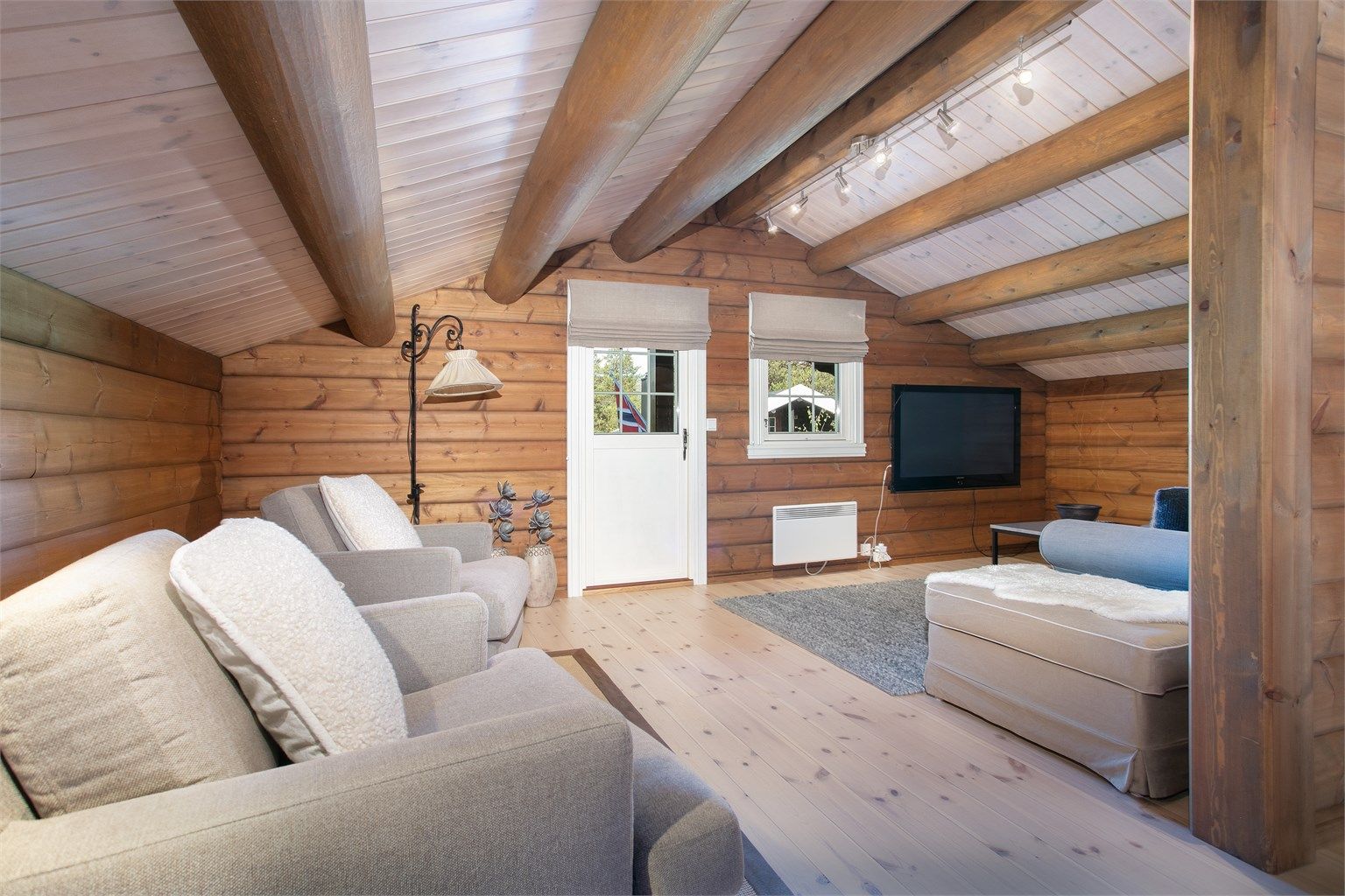 Loftstue med åpen himling, synlige rundåser og dør ut til balkong.