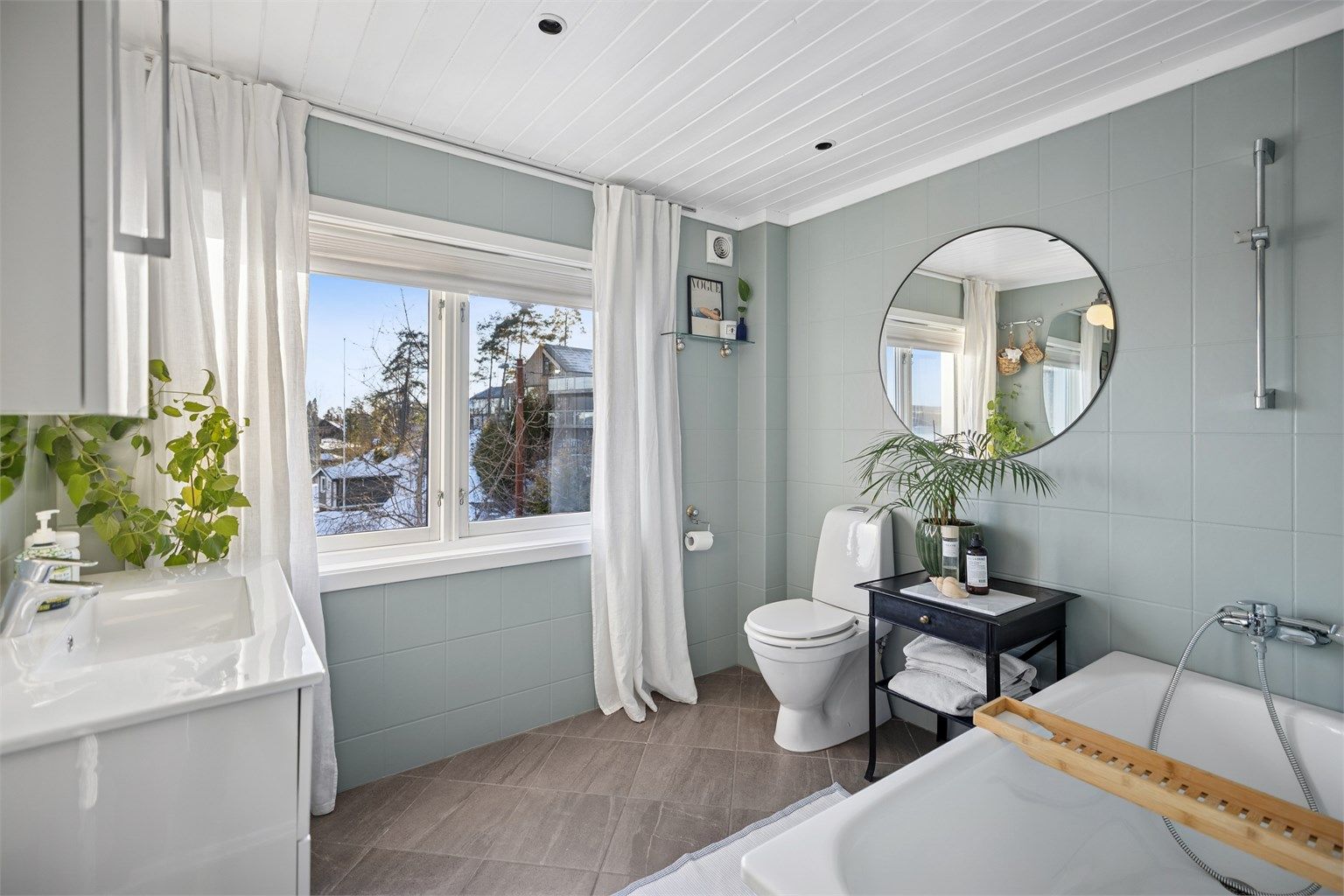 Frittstående badekar med veggmontert dusjarmatur og gulvstående toalett.