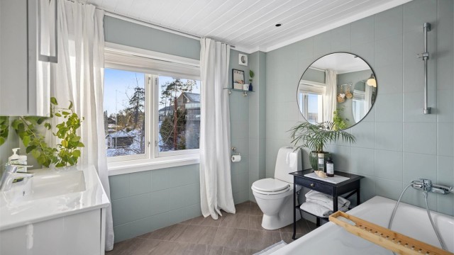 Frittstående badekar med veggmontert dusjarmatur og gulvstående toalett.