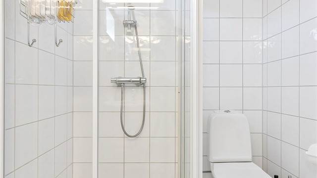 Baderom fra byggeår. Flislagt gulv med gulvvarme. Flislagte vegger. Takplater i himling. Vegghengt servantinnredning. Speil med overlys. Dusjhjørne med dører. Gulvstående toalett.