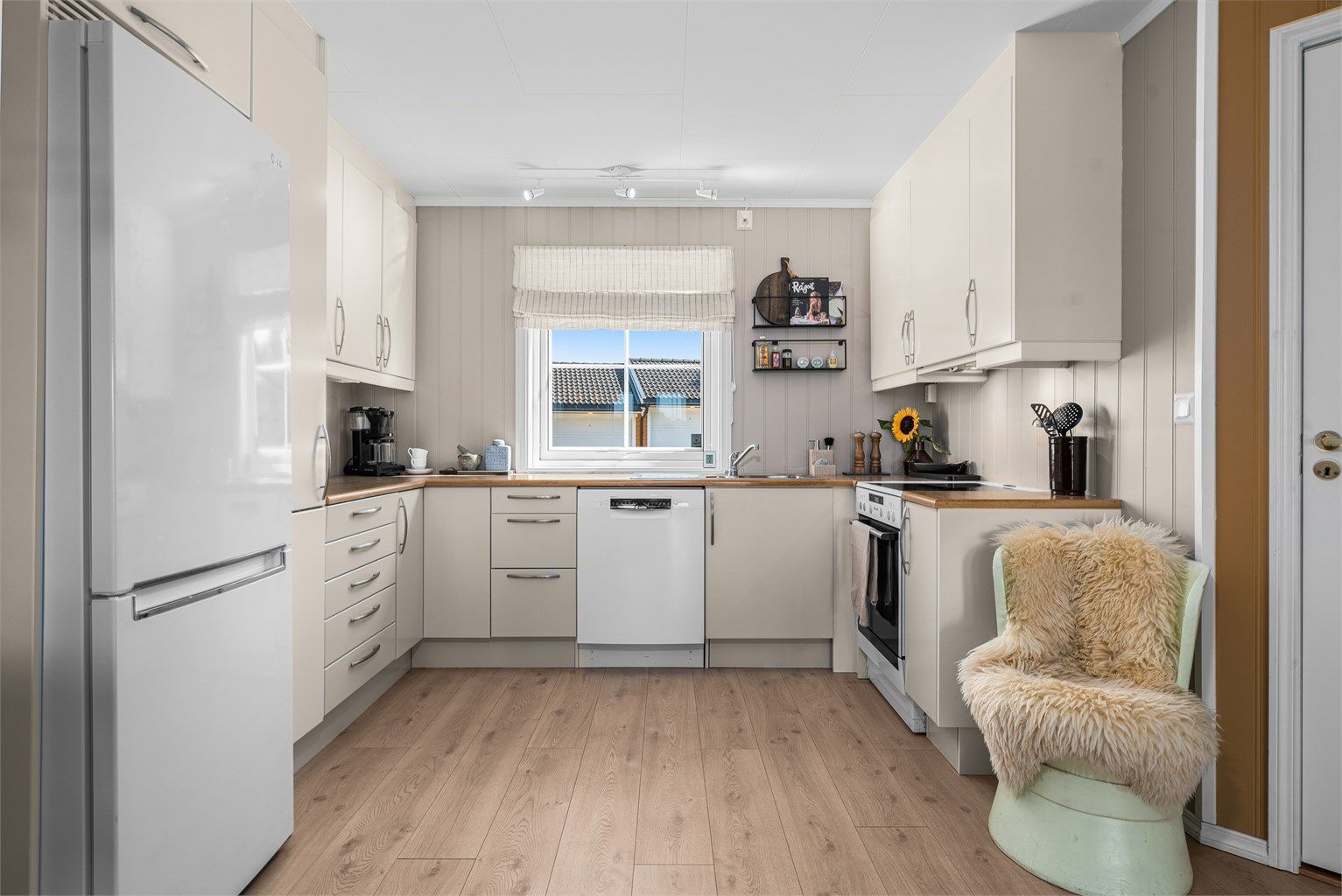 Pent kjøkken med innredning i lyse fronter, laminert benkeplate og frittstående hvitevarer.