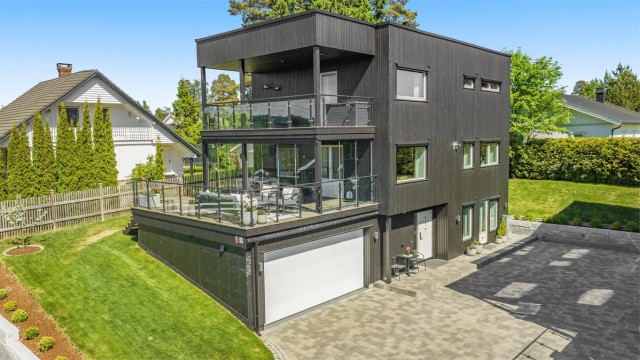 Fasaden har stående bordkledning og et moderne uttrykk med store vindusflater.