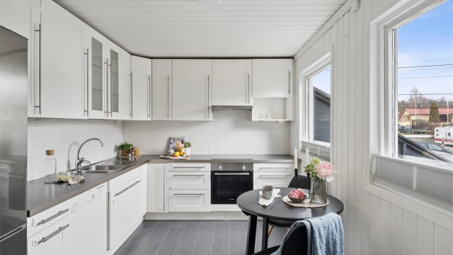 Romslig og lyst kjøkken med innredning med profilerte fronter, laminatbenkeplate, nedfelt oppvaskkum i metall og ettgreps armatur.