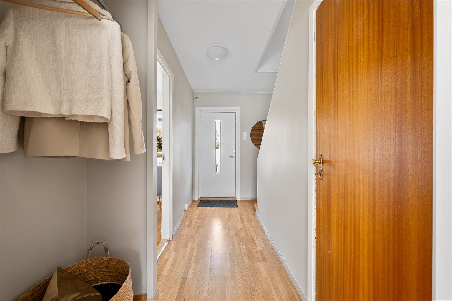 Entré med parkett på gulv, malte vegger i en lys farge og plass til å henge av yttertøy. 