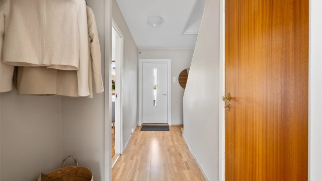 Entré med parkett på gulv, malte vegger i en lys farge og plass til å henge av yttertøy.