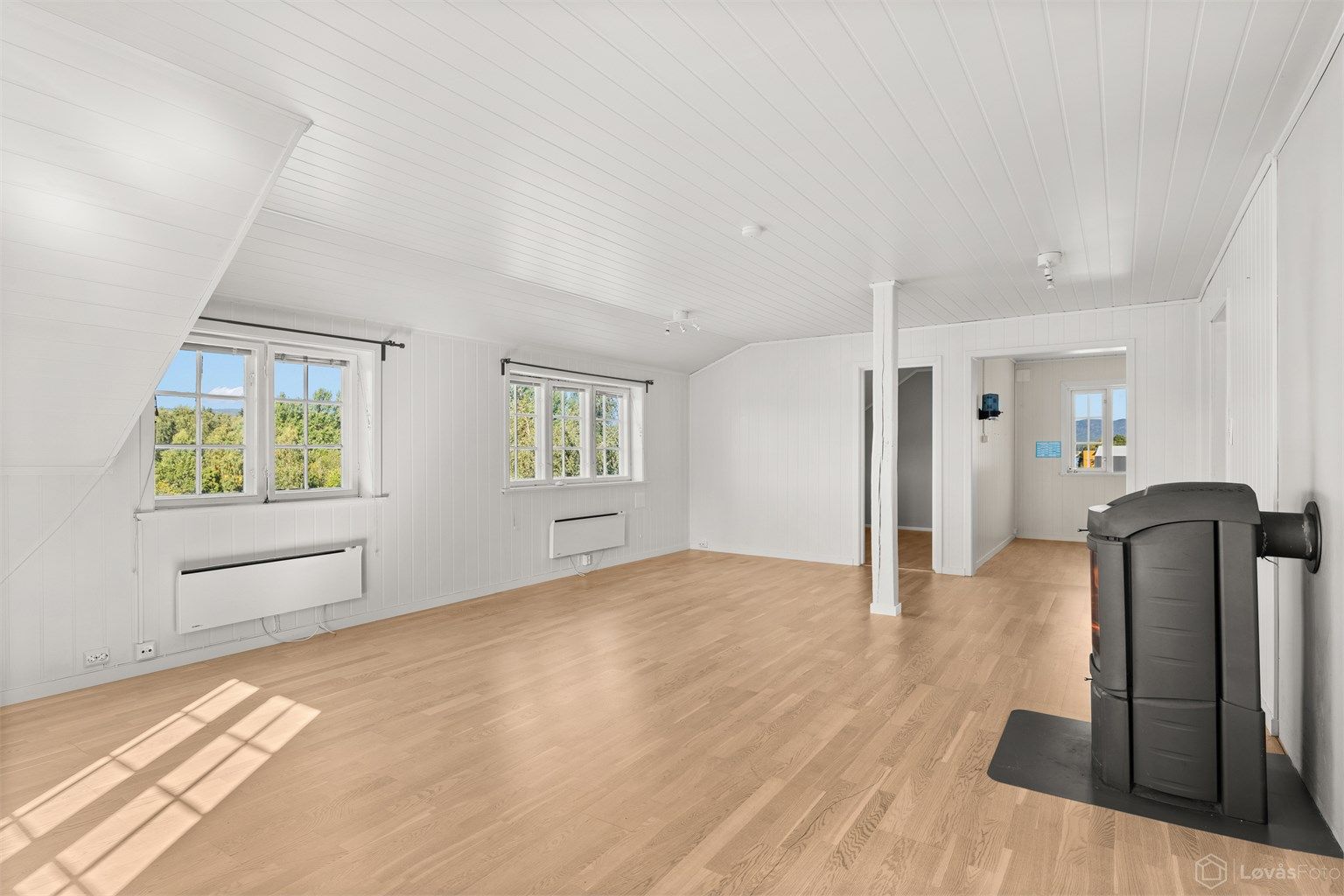 Romslig stue i andre etasje med skråtak, peisovn og godt med naturlig lys.