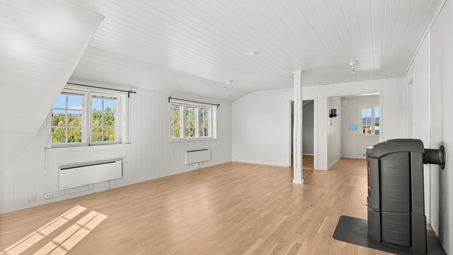 Romslig stue i andre etasje med skråtak, peisovn og godt med naturlig lys.