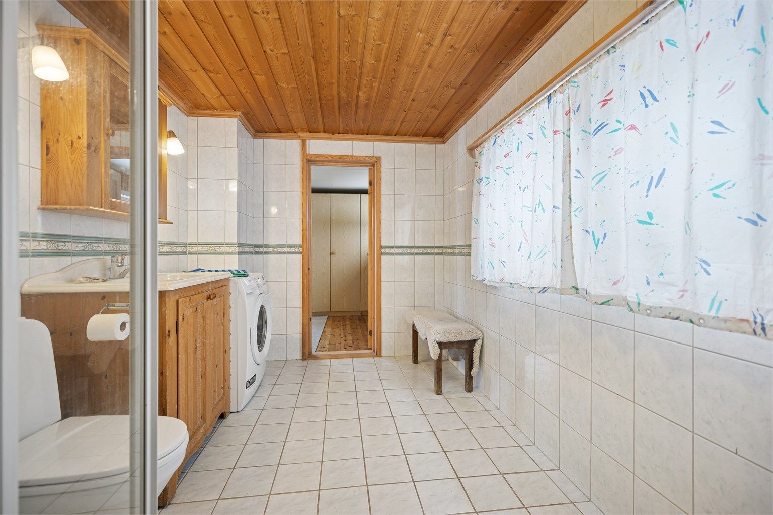 Flislagt bad med gulvvarme, dusjhjørne, servant, gulvstående toalett og opplegg for vaskemaskin