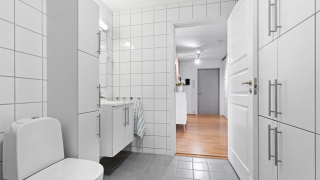 Baderomsinnredning med vegghengt servant, speil med overlys og rikelig med skapplass.