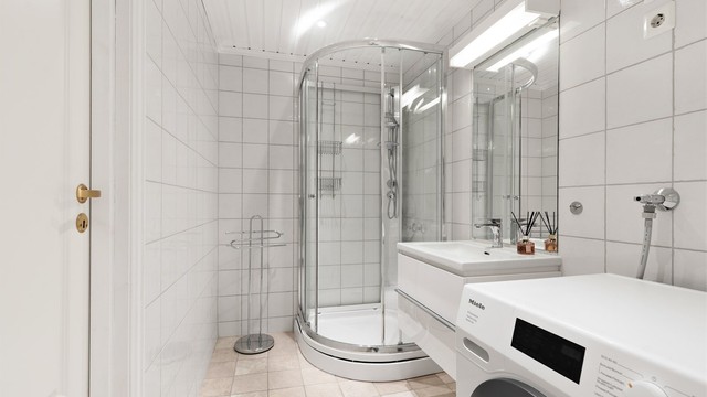Baderommet er innenfor toalettrommet, og har også adkomst via boden i stuen. Her er det gulvvarme, dusjkabinett, vegghengt servantskap og opplegg for vaskemaskin.