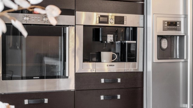 Benkeskapsbelysning og stikkontakter over kjøkkenbenk. Integrert stekeovn, platetopp, oppvaskmaskin, kaffemaskin og kjøleskap med fryser.