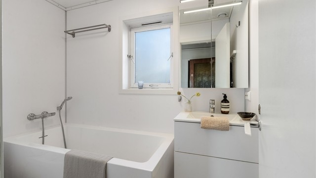 Nyere bad i første etasje med badekar og vegghengt servant.
