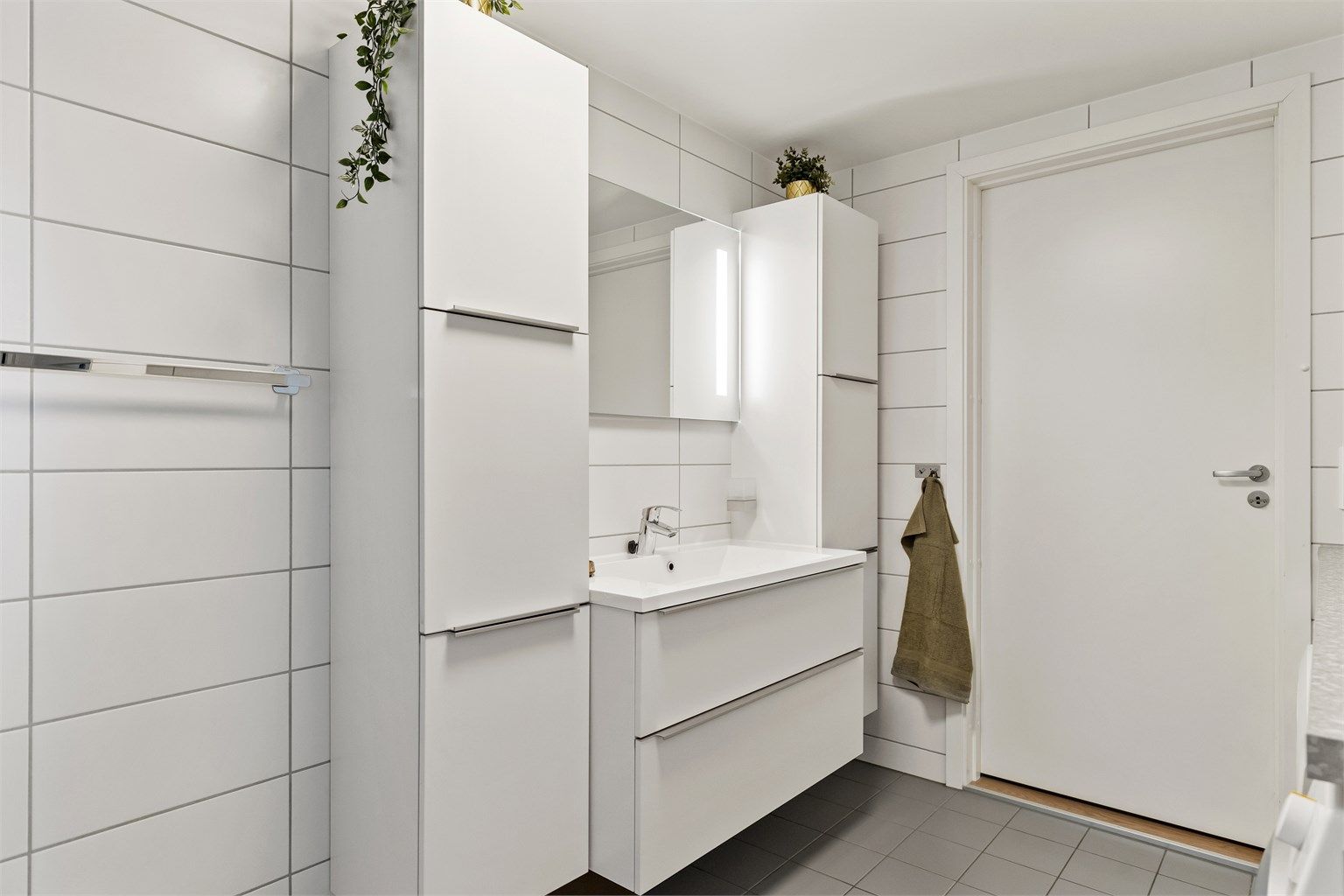 Baderomsinnredning med vegghengt servant, speil med belysning og rikelig med skapplass.