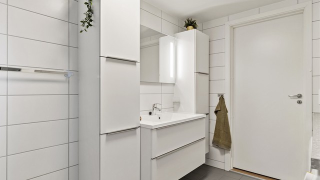 Baderomsinnredning med vegghengt servant, speil med belysning og rikelig med skapplass.