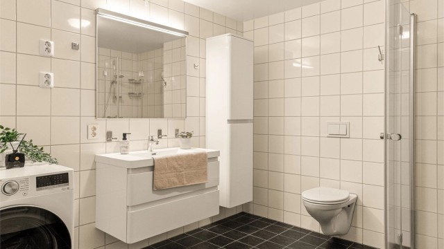 Pent flislagt bad med vegghengt toalett, foldbare dusjdører og god oppbevaring. Opplegg for vaskemaskin og plass til tørketrommel i rommet.
