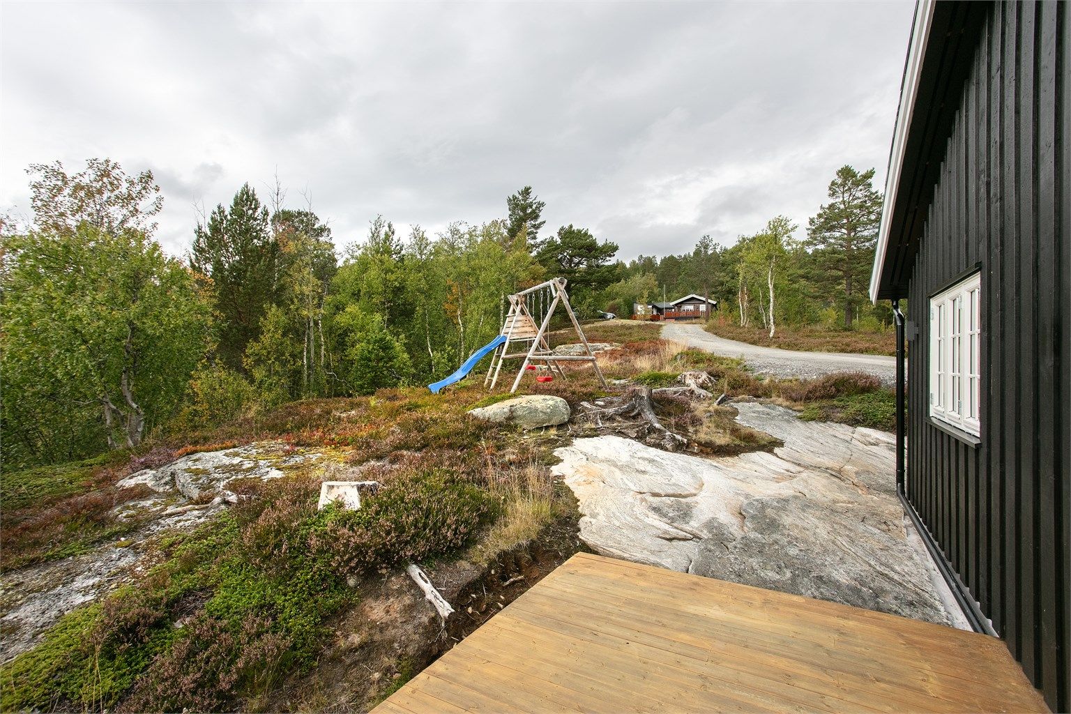 Tomten er opparbeidet med naturlig fjellbunn, lyng og lekeplass.
