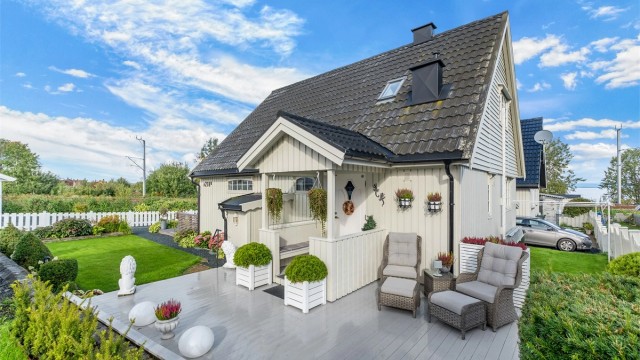 Fasade kledd med trepanel og pent opparbeidet hage med plen og beplantning.