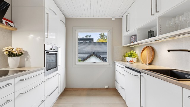 Kjøkkenet ligger i eget rom og har hvit innredning med rikelig benkeplass.