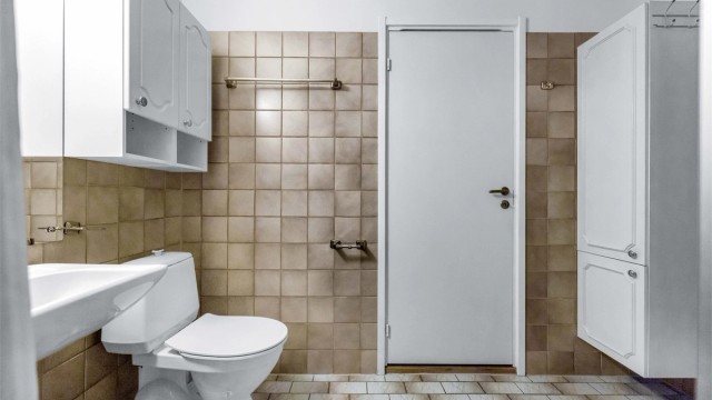 Badet er innredet med dusj, gulvstående toalett, vegghengt servant med armatur., speil og baderomsinnredning med hvite profilerte fronter.