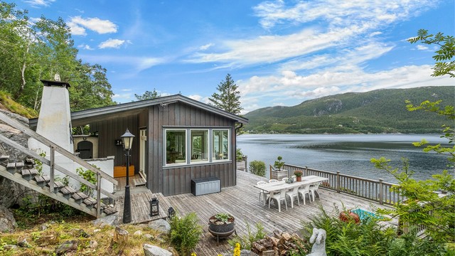 Hytta ligger flott til i terrenget med terrassen vendt mot sjøen og fjellandskapet på motsatt side.