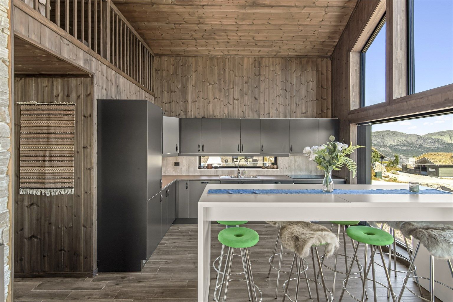 Kjøkkenet er et stilrent Huseby-kjøkken med åpen løsning mot stuen. Her er det flislagt gulv med gulvvarme, beiset trepanel på vegger og himling, slette fronter, laminert benkeplate og nedfelt oppvaskkum i metall. 