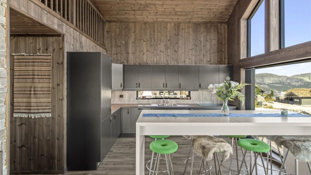 Kjøkkenet er et stilrent Huseby-kjøkken med åpen løsning mot stuen. Her er det flislagt gulv med gulvvarme, beiset trepanel på vegger og himling, slette fronter, laminert benkeplate og nedfelt oppvaskkum i metall.