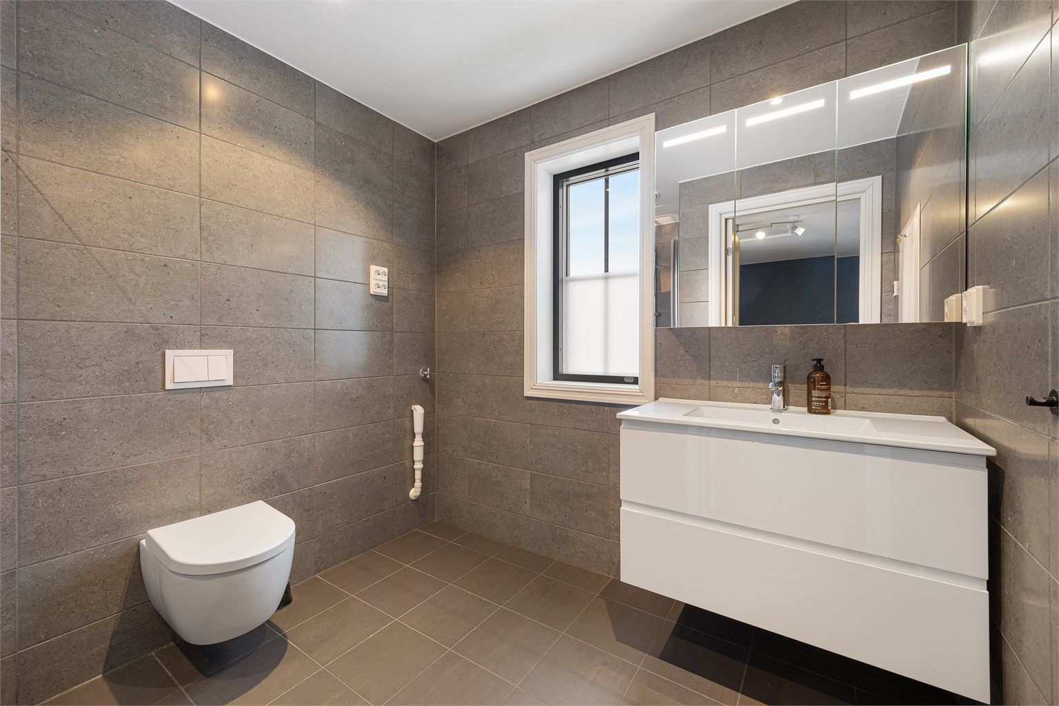 Delikat, flislagt bad med vegghengt toalett og servantinnredning med gode skuffer.