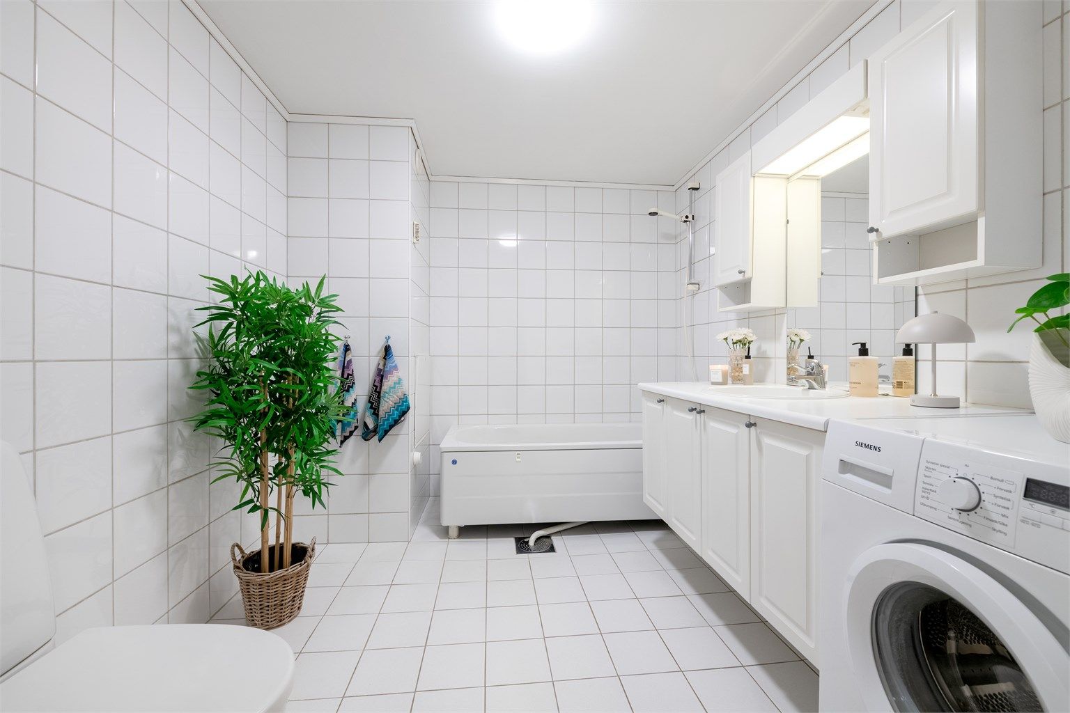 Badet er romslig og lyst med hvit baderomsinnredning og badekar. Fordelerskap for rør-i-rør system er plassert på bad. 