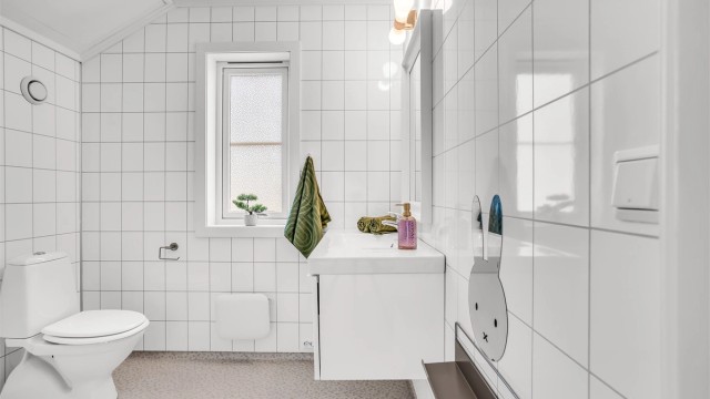 Bad i loftsetasjen med servantinnredning, speil med belysning og frittstående toalett. Gulv med gulvbelegg og våtromsplater på veggene.