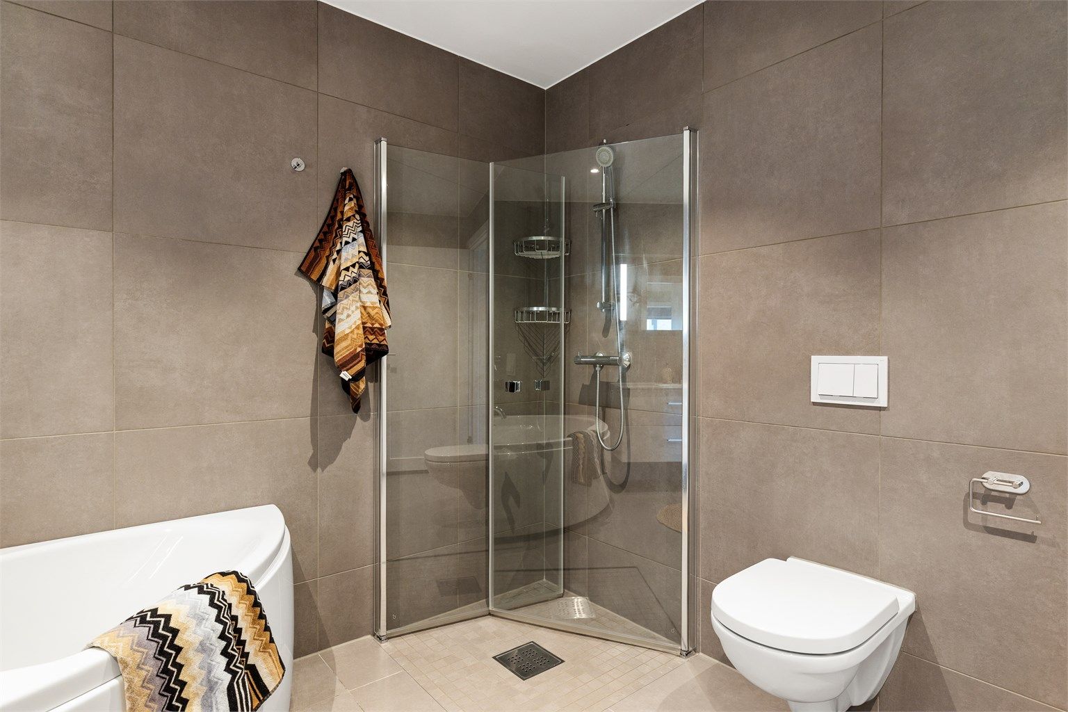 Badet er utstyrt med vegghengt toalett og dusjplass med inn- og utadslående dusjvegger.