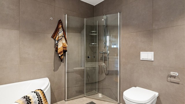 Badet er utstyrt med vegghengt toalett og dusjplass med inn- og utadslående dusjvegger.