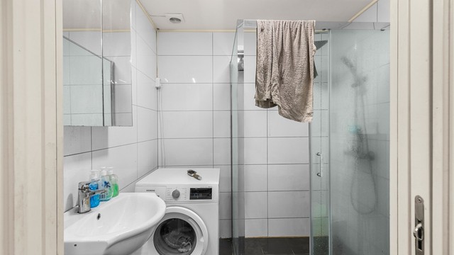 Flislagt bad på 3,5 kvm innredet med servantskap med speil, toalett, dusjhjørne og opplegg for vaskemaskin. Badet er opprinnelig byggemeldt som en del av garasjen. Det er ikke søkt bruksendring fra tilleggsdel til hoveddel.
