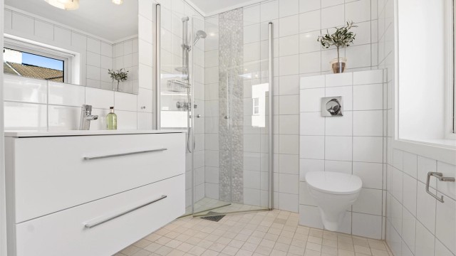 Lekkert flislagt bad med dusjsone og praktiske innfellbare dører. I tillegg er det vegghengt toalett og stilrent baderomsmøbel. Alt i lyse og moderne materialer