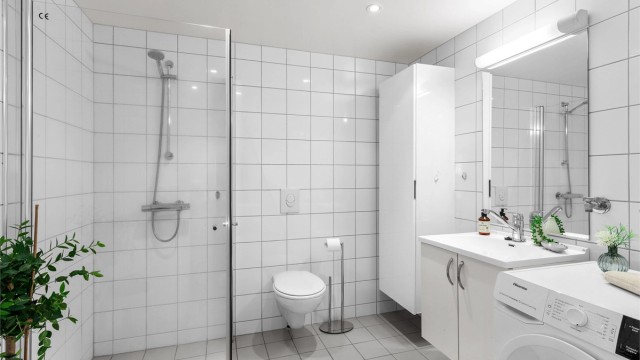 Flislagt bad med gulvvarme. Himling med downlights. Vegghengt servantinnredning med ovenpåliggende servant. Dusjhjørne med dører i glass.