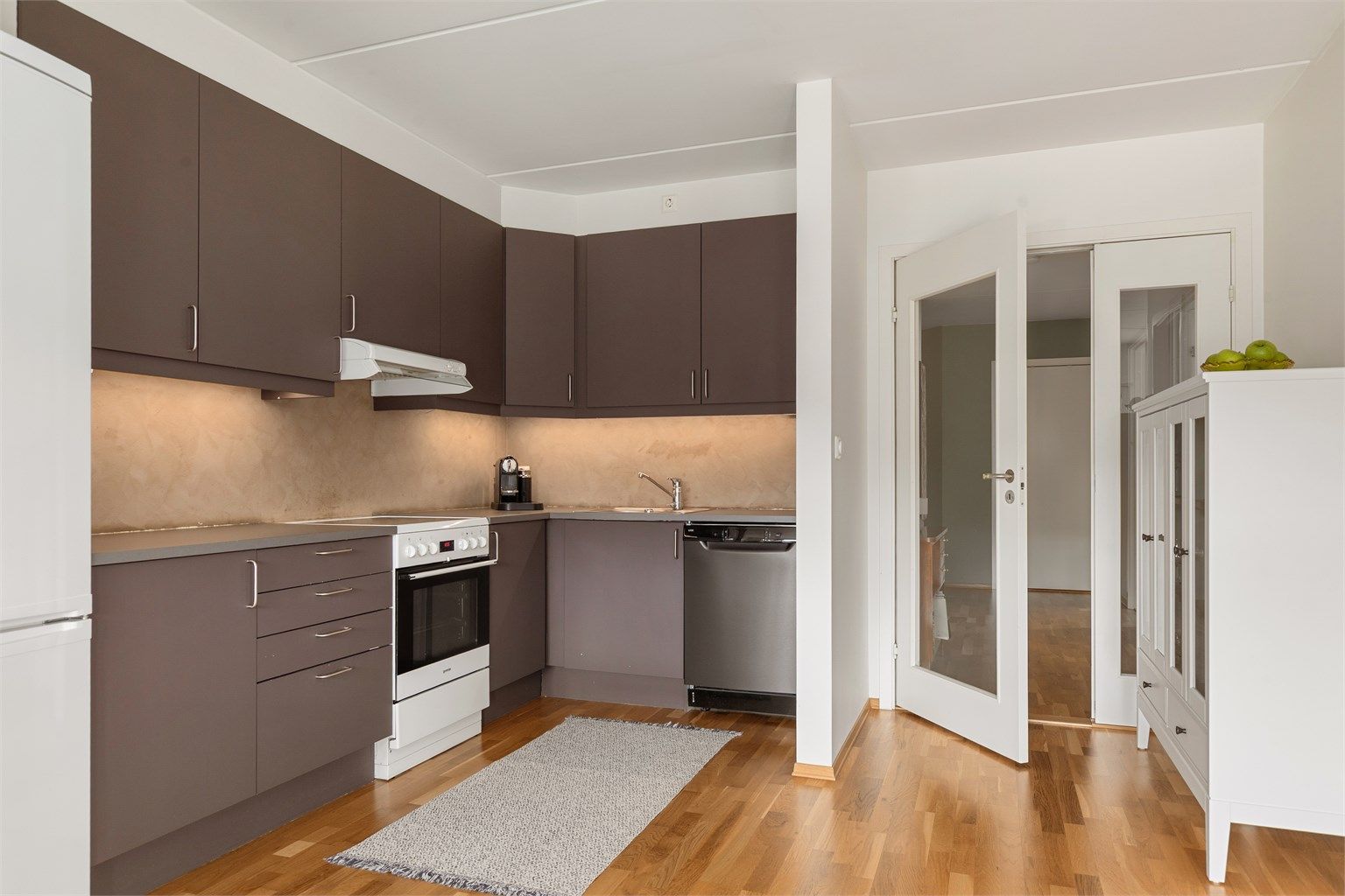 Kjøkken innredet med over- og underskap i grå slette fronter med frittstående hvitevarer. Disse medfølger salget.