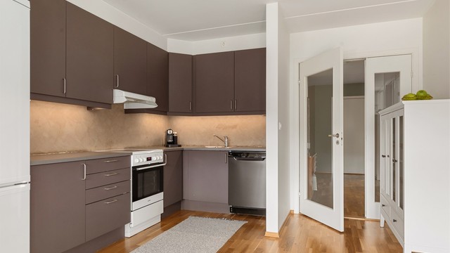 Kjøkken innredet med over- og underskap i grå slette fronter med frittstående hvitevarer. Disse medfølger salget.