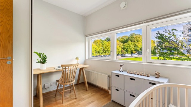 Arbeidsplass plassert foran vinduet med utsikt mot trekronene utenfor.