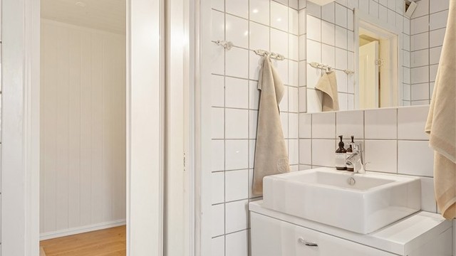Flislagt bad med gulvvarme, vegghengt servantinnredning og speil med overlys.