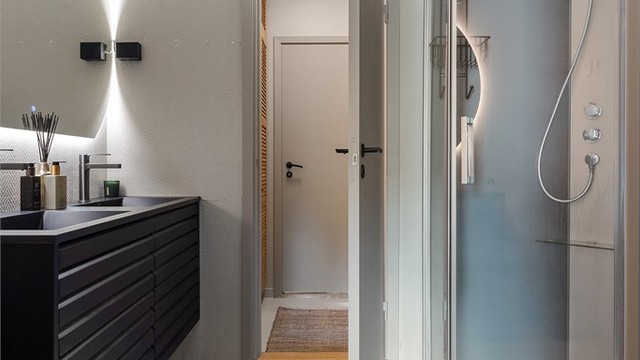 Baderom med flislagt gulv. Tapet på vegger. Malte flater i himling. Dobbel ovenpåliggende servant med armaturer. Speil med sidelys. Dusjkabinett med dusjarmatur. Mekanisk avtrekk med ventil i vegg. TIlgang fra entré og fra hovedsoverommet.