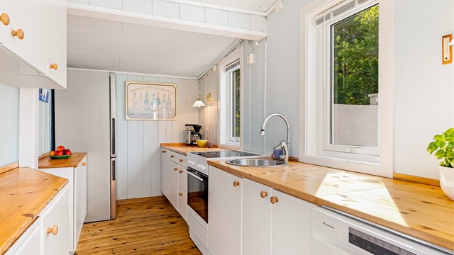 Innredningen har slette fronter og benkeplate i treverk. Det er rikelig med benkeplass. Det er plass til kjøleskap, oppvaskmaskin og komfyr.
