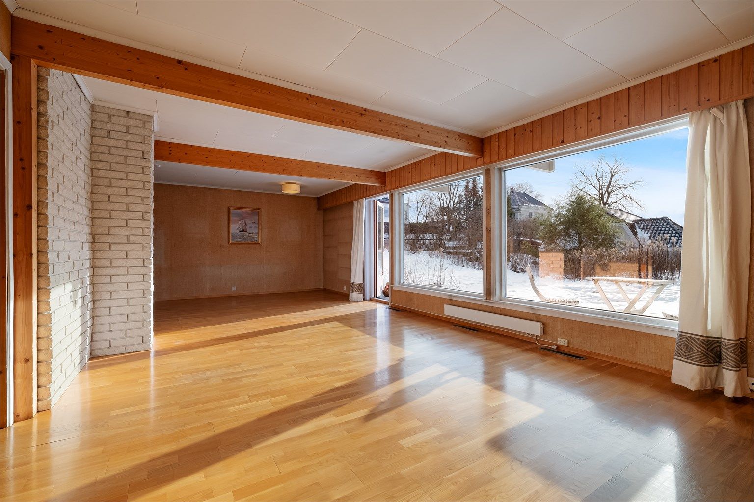 Boligens oppholdsrom fremstår åpent, luftig og lyst med store vinduer og mye naturlig lys ettersom rommet vender mot syd.