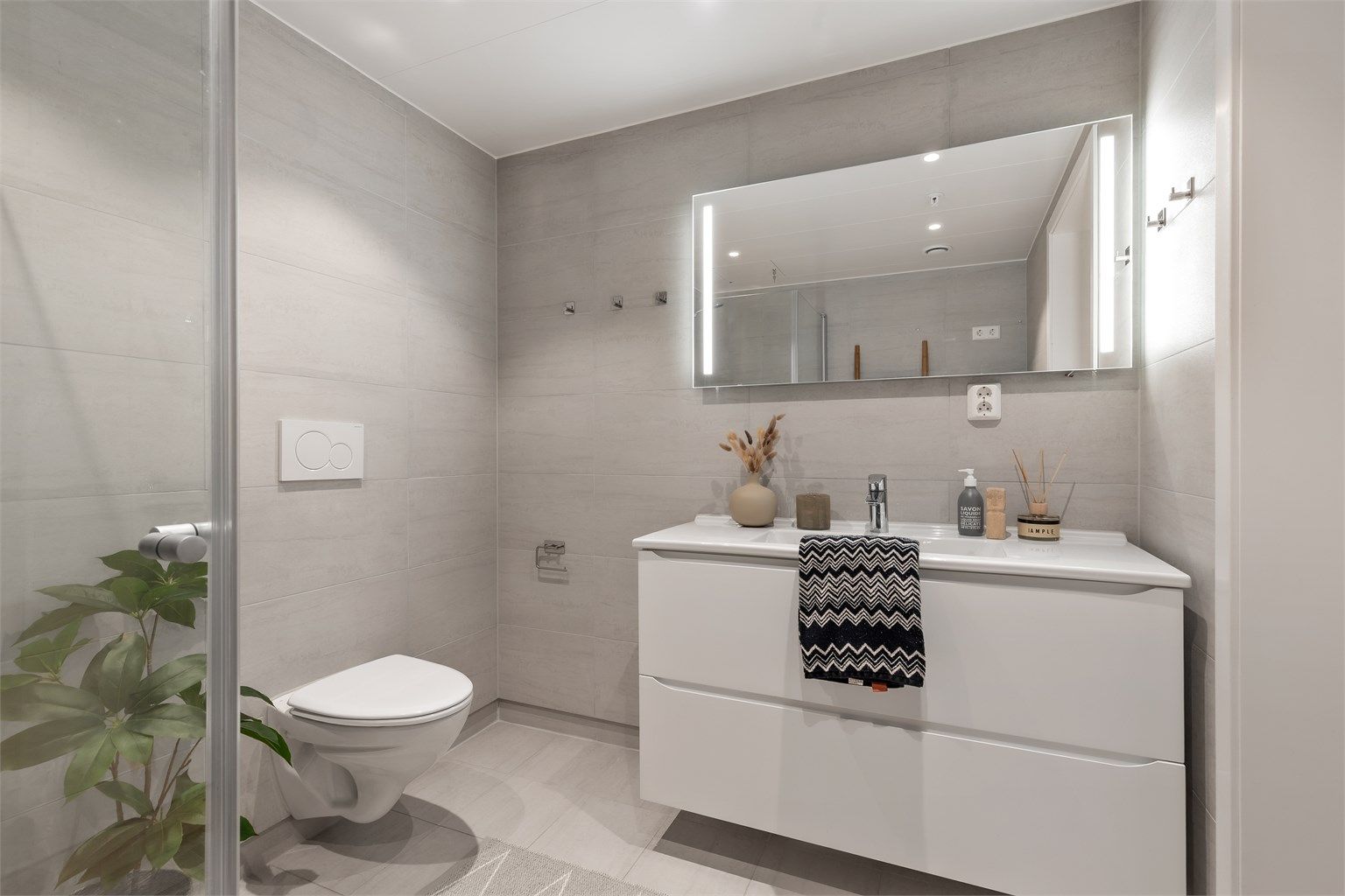 Servant med ett-greps armatur og speil. Dusjhjørne med dusjarmatur. Innebygd sisterne med vegghengt toalett.