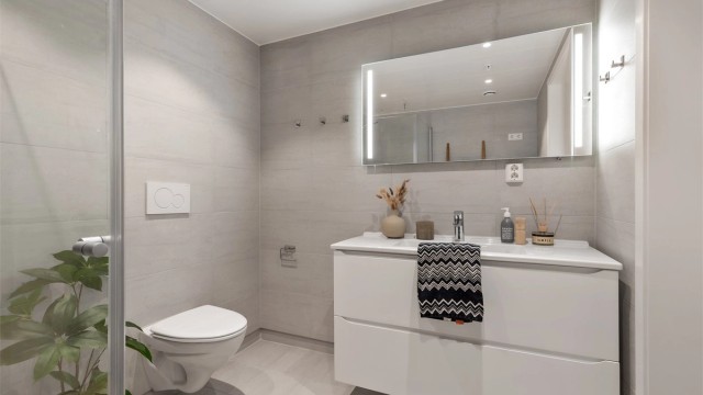 Servant med ett-greps armatur og speil. Dusjhjørne med dusjarmatur. Innebygd sisterne med vegghengt toalett.