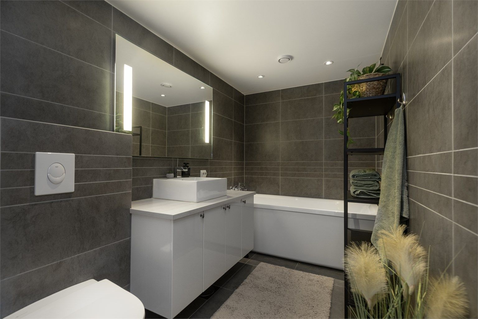 Moderne flislagt bad med mørke fliser, stilrene overflater og funksjonell innredning. Badet tilbyr blant annet vannbåren gulvvarme, stemningsfull belysning med downlights.