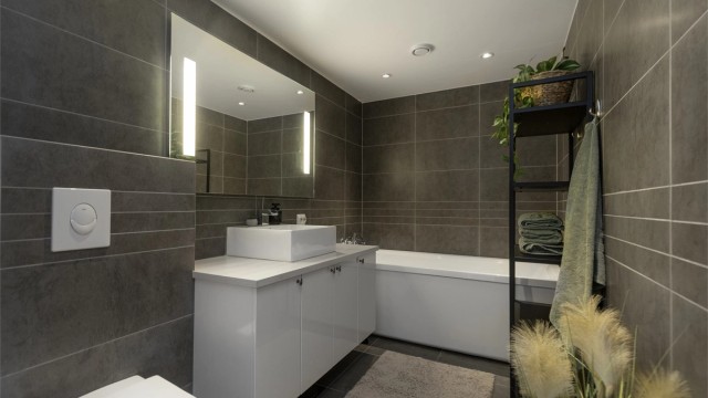 Moderne flislagt bad med mørke fliser, stilrene overflater og funksjonell innredning. Badet tilbyr blant annet vannbåren gulvvarme, stemningsfull belysning med downlights.