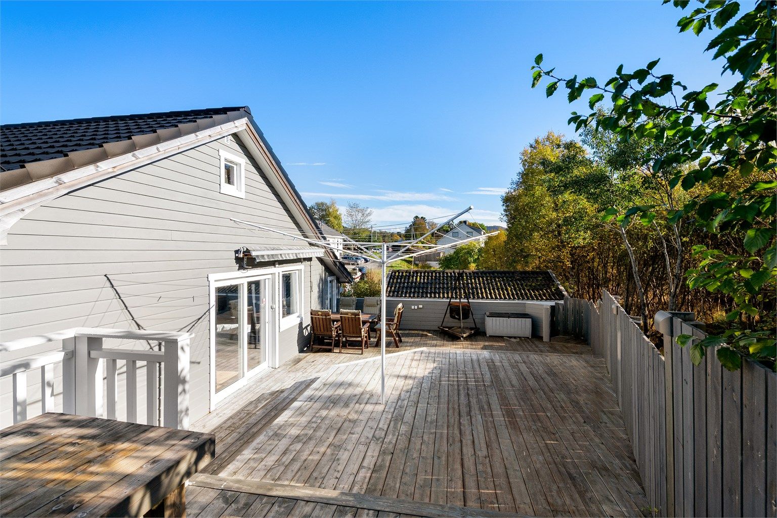 Terrasse i trekonstruksjon med rekkverk og levegg mot tomtegrensen.