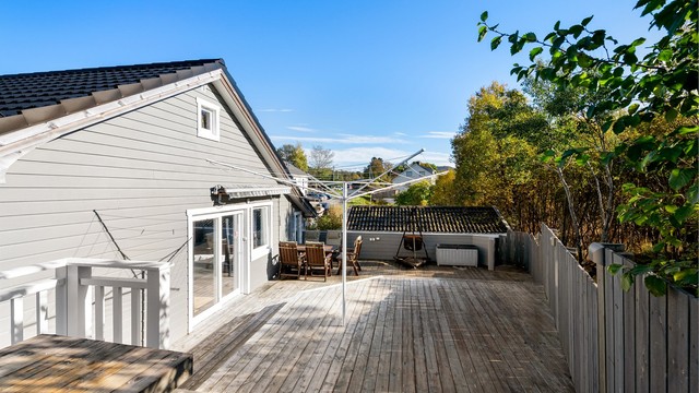 Terrasse i trekonstruksjon med rekkverk og levegg mot tomtegrensen.