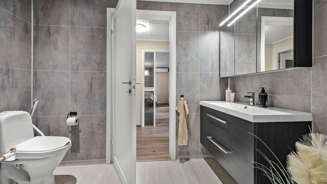 Badet er innredet med vegghengt servantinnredning, speilskap, gulvstående toalett, dusjhjørne og opplegg for vaskemaskin